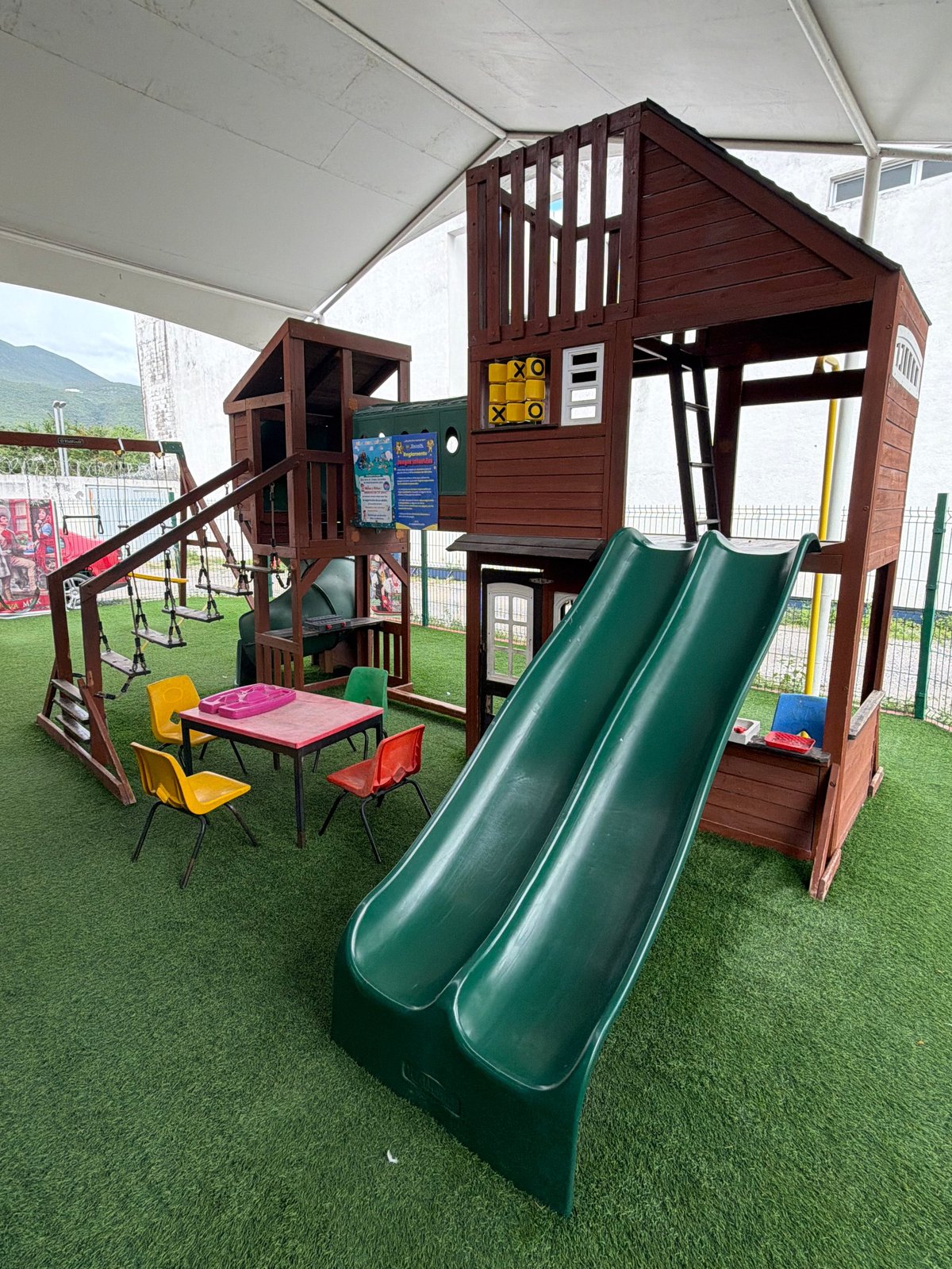 Casita de juegos de madera con dos toboganes verdes y mesita para niños en Tecuán