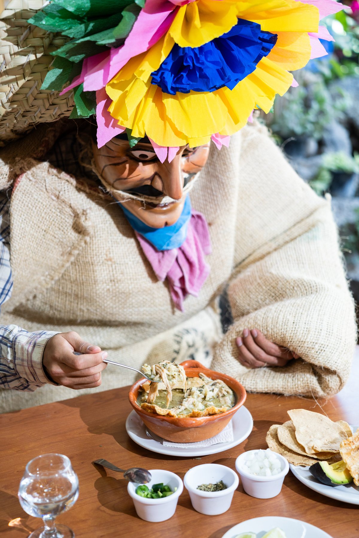 Tlacololero con corona de flores de papel comiendo pozole en mesa de madera